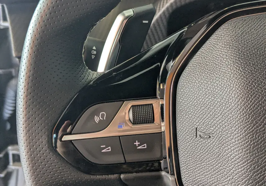 Gros plan sur les commandes gauche du volant en cuir perforé noir du Peugeot 208 Hybrid 145 e-DCS6 GT 2025.