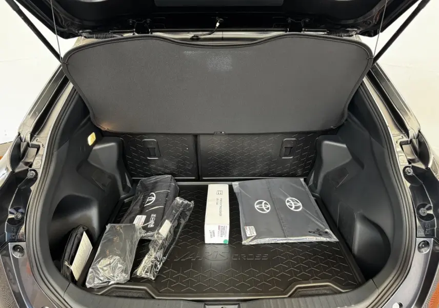 Coffre ouvert d’une Toyota Yaris Cross gris foncé, vue arrière, avec accessoires d’origine posés à l’intérieur.