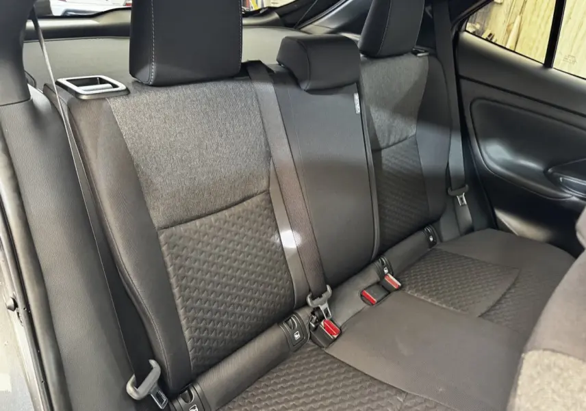 Vue intérieure de la banquette arrière grise foncée de la Toyota Yaris Cross 1.5 Hybrid 130h Design Auto, avec ceintures et appuie-têtes.