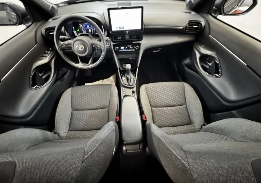 Vue intérieure avant de la Toyota Yaris Cross 1.5 Hybrid 130h, sièges gris et tableau de bord avec écran tactile central.