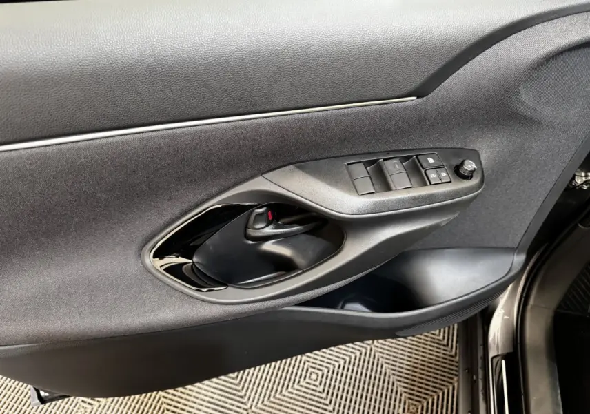 Gros plan sur la porte avant gauche de la Toyota Yaris Cross 2026 gris foncé, montrant les commandes des vitres et la poignée intérieure.