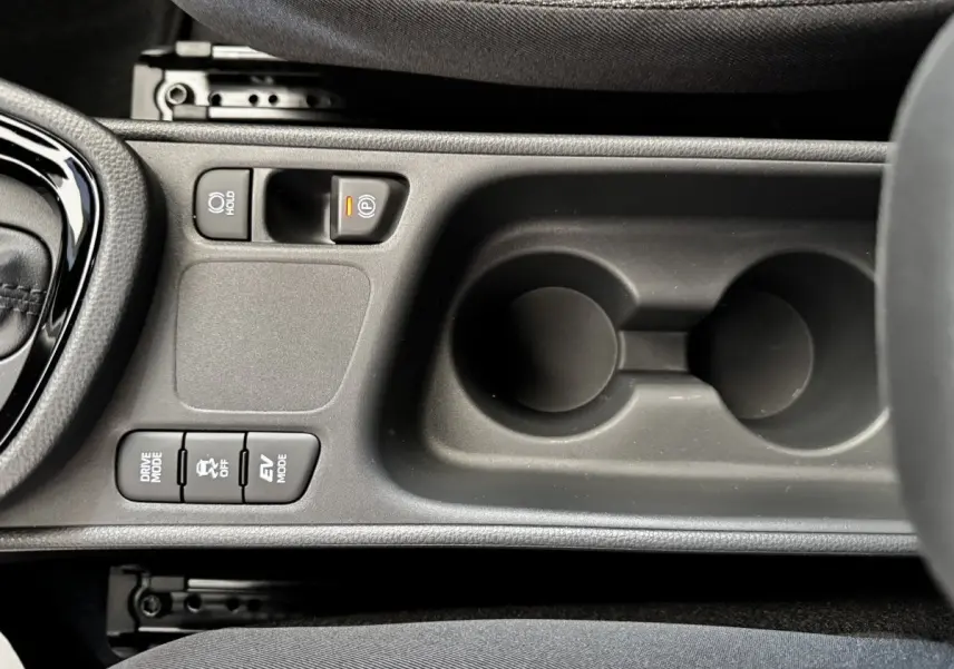 Vue en plongée sur la console centrale noire de la Toyota Yaris Cross 2026, avec boutons de mode de conduite et frein électrique.