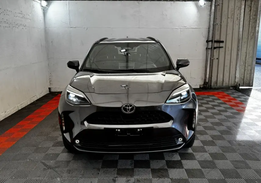 Vue frontale d'une Toyota Yaris Cross 1.5 Hybrid 130h Design Auto gris foncé avec phares LED allumés dans un garage.