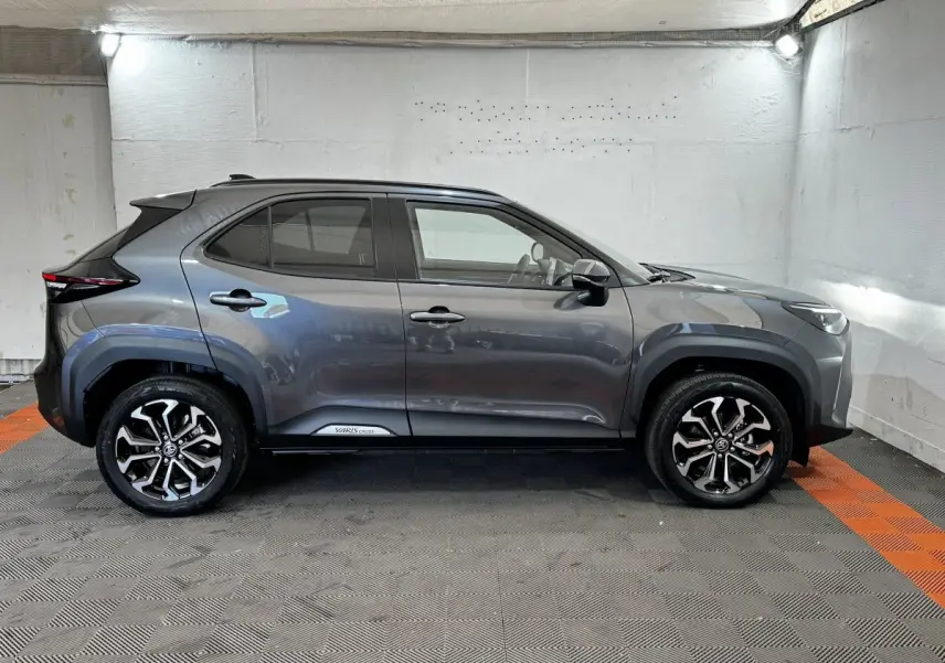 Vue de profil droit d'un Toyota Yaris Cross gris foncé avec jantes alliage bicolores et protections noires sur les passages de roues.