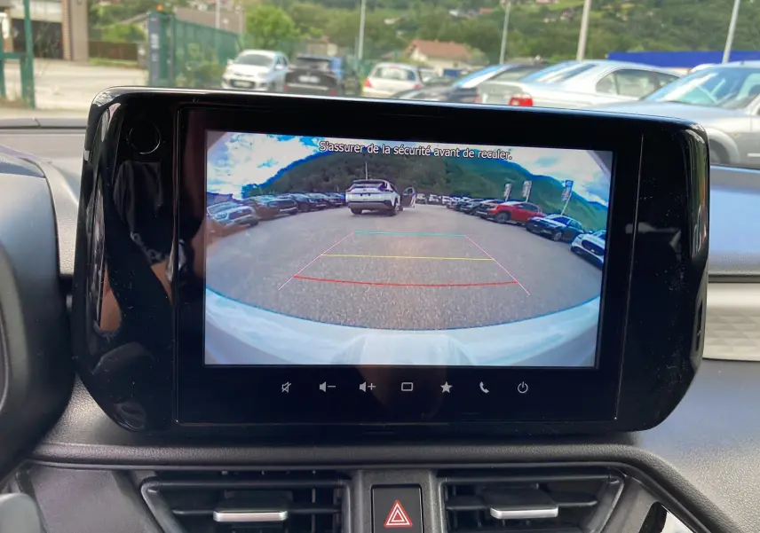 Écran central affichant la caméra de recul d'une Suzuki Swift blanche, vue depuis l'intérieur avant.