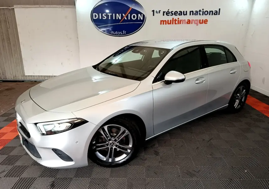 Vue 3/4 avant droite d'une Mercedes Classe A A 180 d Business Line gris clair, avec jantes alliage et phares LED allumés.