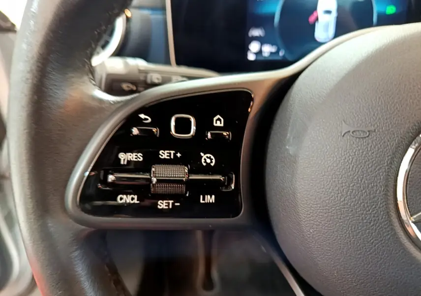 Gros plan sur les commandes de régulateur de vitesse au volant cuir d’une Mercedes Classe A gris clair de 2020.