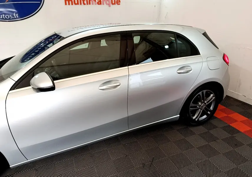 Vue de profil côté gauche d'une Mercedes Classe A gris clair garée en intérieur sur sol à damier noir et rouge.