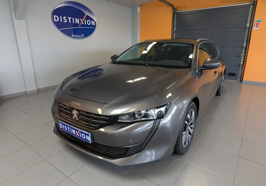 Peugeot 508 SW gris en 3/4 avant droit dans un showroom avec logo Distinxion en arrière-plan.