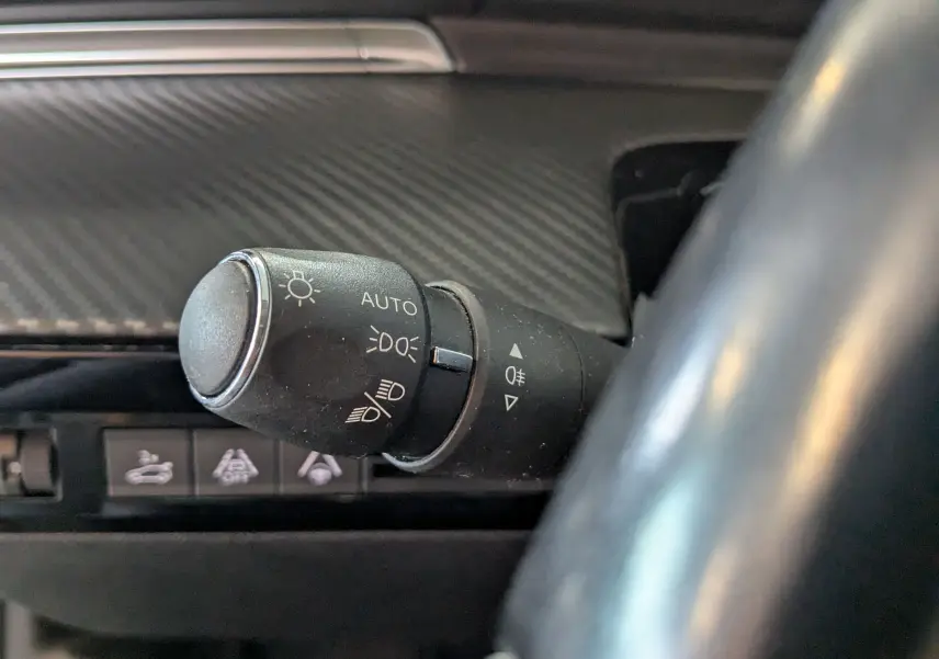 Gros plan sur la commande des phares à gauche du volant dans l’habitacle gris carbone d’une Peugeot 508 SW 2021.
