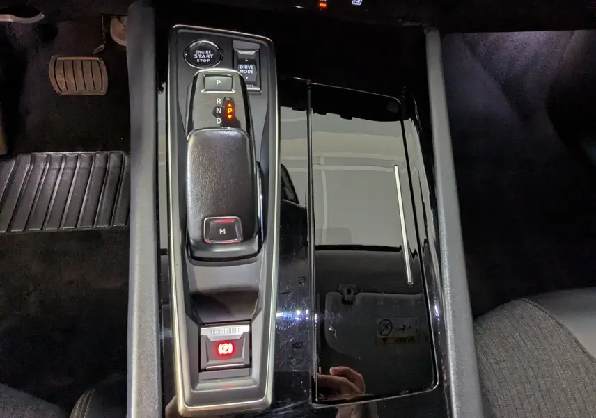 Vue rapprochée de la console centrale noire brillante avec levier de vitesse automatique et bouton start/stop d'une Peugeot 508 SW 2021.