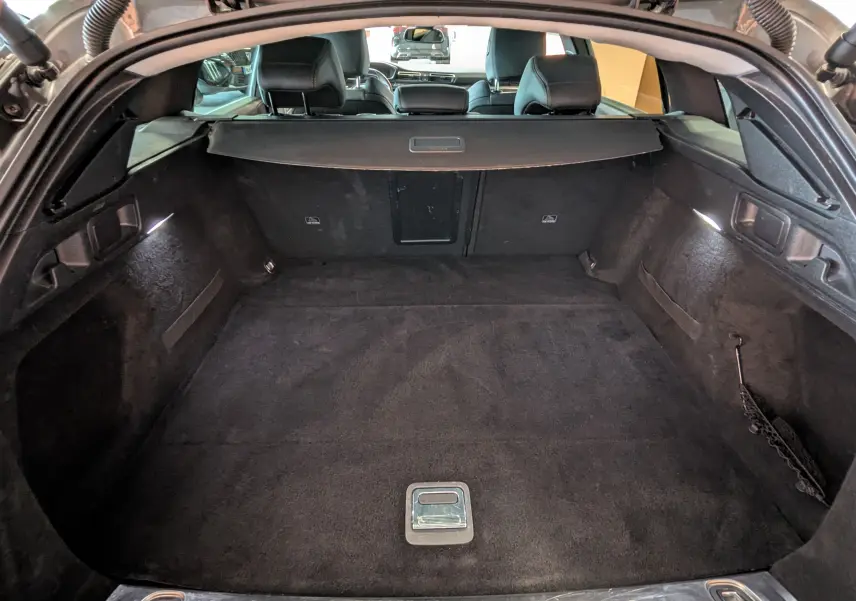 Coffre ouvert vu de l'arrière d'une Peugeot 508 SW gris, montrant un espace de chargement propre et bien éclairé.