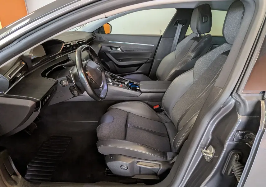 Vue intérieure côté conducteur de la Peugeot 508 SW gris 2021, sièges tissu gris et cuir avec tableau de bord moderne.