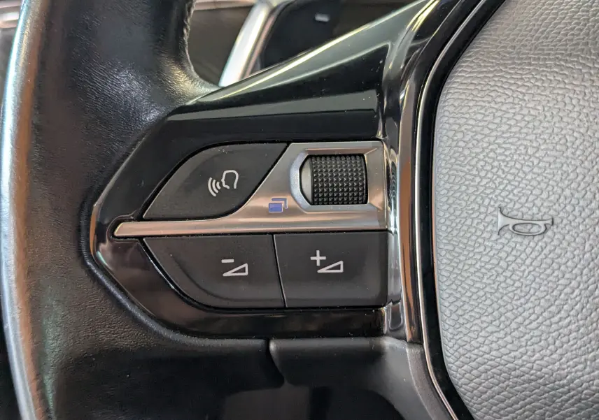 Gros plan sur les commandes de volume et téléphone intégrées au volant noir du Peugeot 508 SW gris, version 2021.