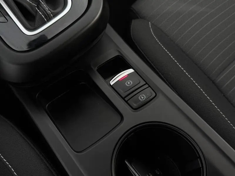 Gros plan sur la console centrale noire du Renault Arkana 2025, montrant les boutons de frein à main et arrêt auto, siège tissu gris.