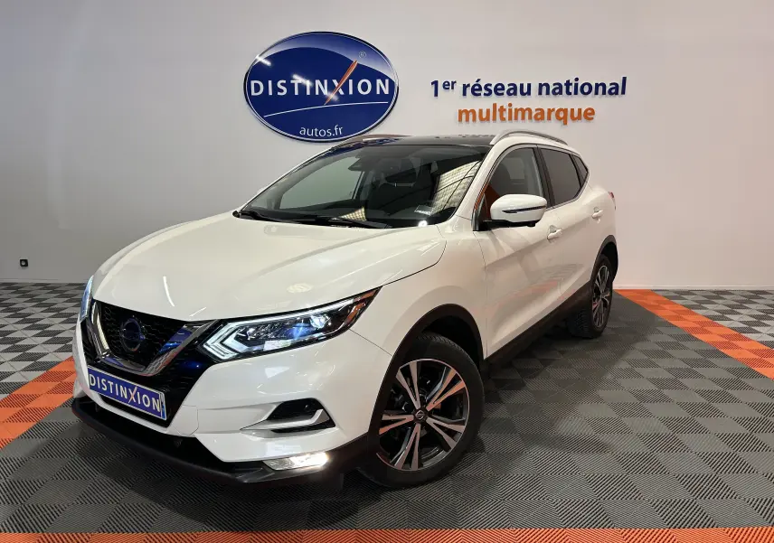Nissan Qashqai blanc en 3/4 avant droit, avec toit panoramique et jantes alliage bicolores visibles.
