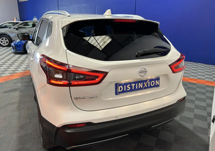 Vue 3/4 arrière d'un Nissan Qashqai blanc avec feux arrière allumés dans un showroom.