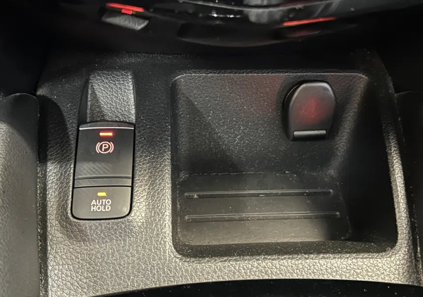 Gros plan sur la console centrale noire du Nissan Qashqai 1.6 dCi avec bouton frein à main électronique et rangement.