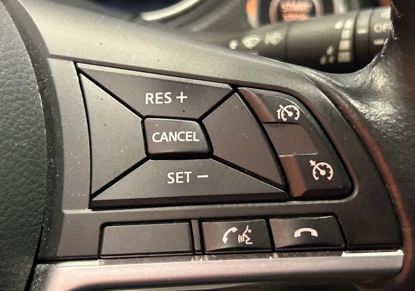 Gros plan sur les commandes de régulateur de vitesse et téléphone au volant en cuir noir du Nissan Qashqai blanc 2018.