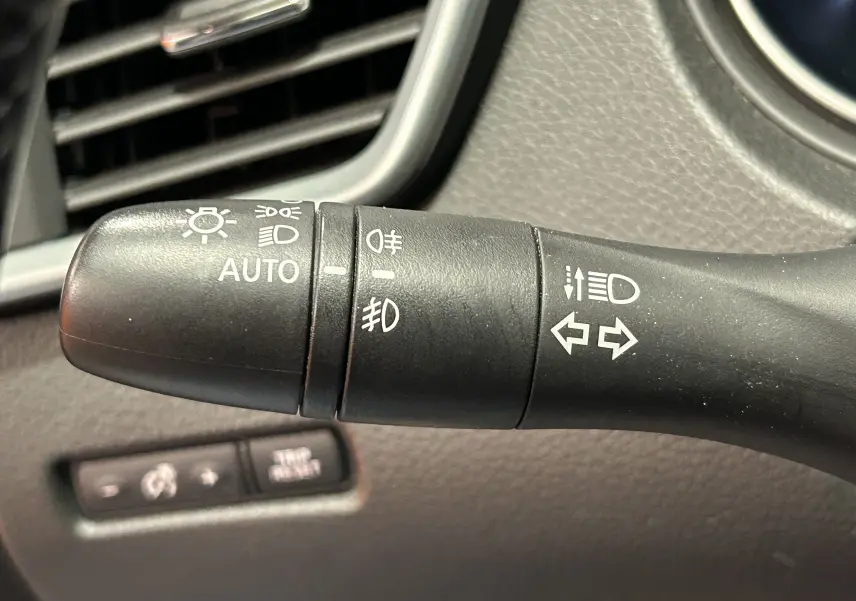 Gros plan sur la commande des phares et clignotants du Nissan Qashqai blanc, intérieur en plastique noir texturé.