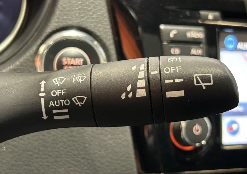 Gros plan sur la commande d’essuie-glace noire dans l’habitacle du Nissan Qashqai blanc, avec bouton start en arrière-plan flou.