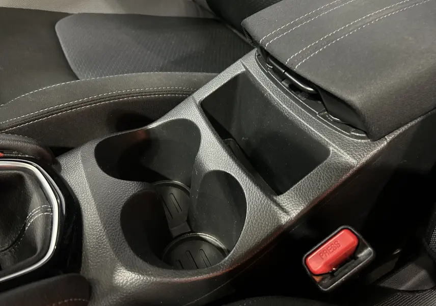 Gros plan sur la console centrale noire avec porte-gobelets et bouton de ceinture rouge dans un Nissan Qashqai 2018.