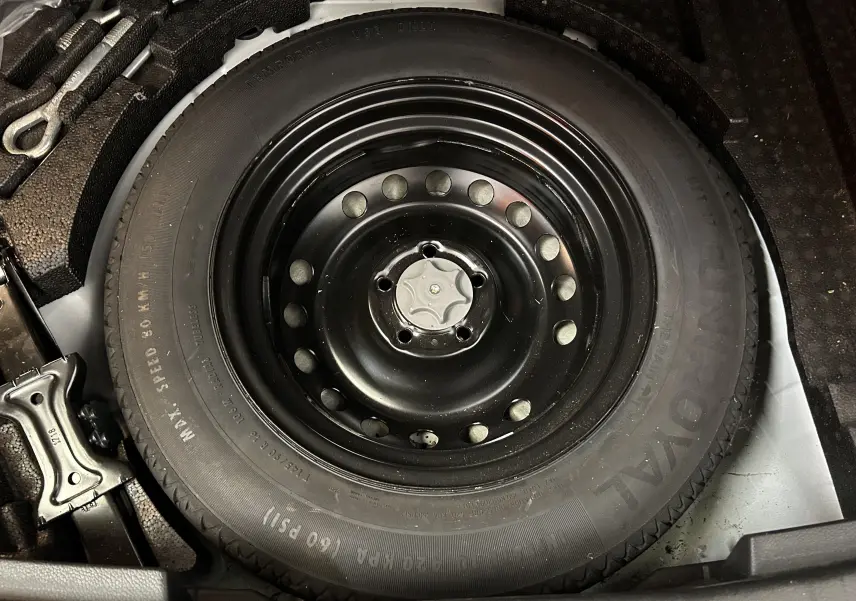 Gros plan sur la roue de secours noire en acier du Nissan Qashqai blanc, visible dans le coffre.