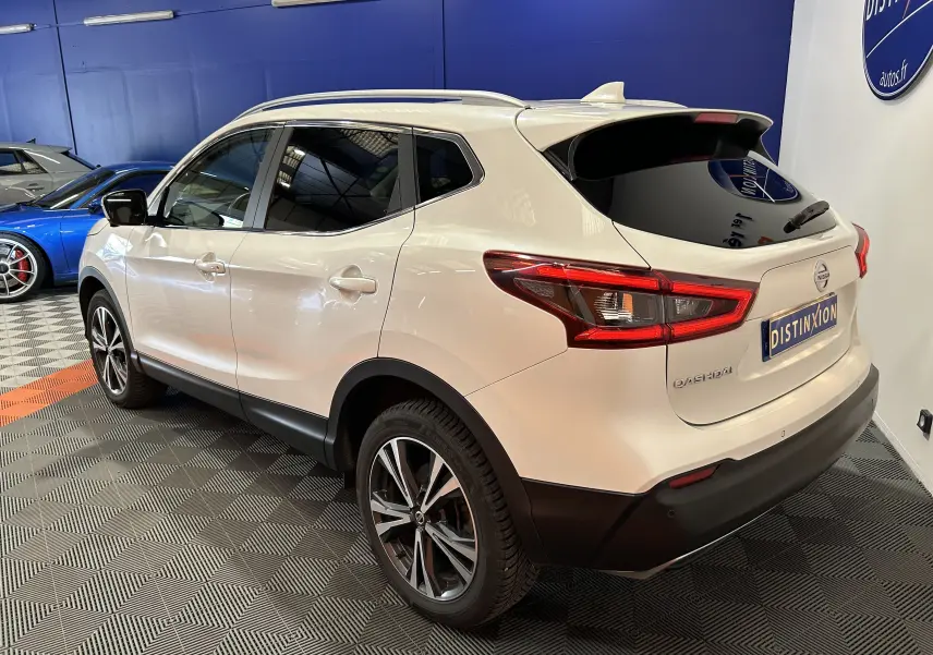 Vue 3/4 arrière droite du Nissan Qashqai blanc avec toit panoramique et jantes alliage en intérieur showroom.