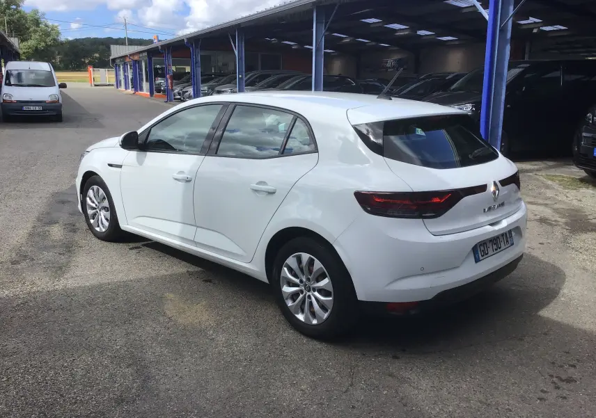 Vue 3/4 arrière droite d’une Renault Mégane IV Société blanche, avec feux arrière allongés et jantes alliage, stationnée en extérieur.