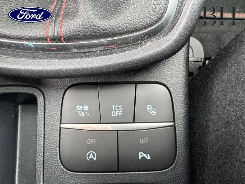 Gros plan sur les boutons de commande du Ford Puma 2023, avec cuir noir et surpiqûres rouges visibles en haut.
