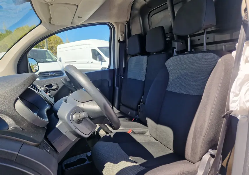Vue intérieure côté conducteur du Renault Kangoo blanc 2021, montrant les sièges tissu noir et gris et le tableau de bord.