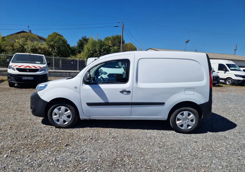Vue de profil côté gauche d’un Renault Kangoo blanc 2021 utilitaire avec poignées et protections noires sur fond extérieur ensoleillé.