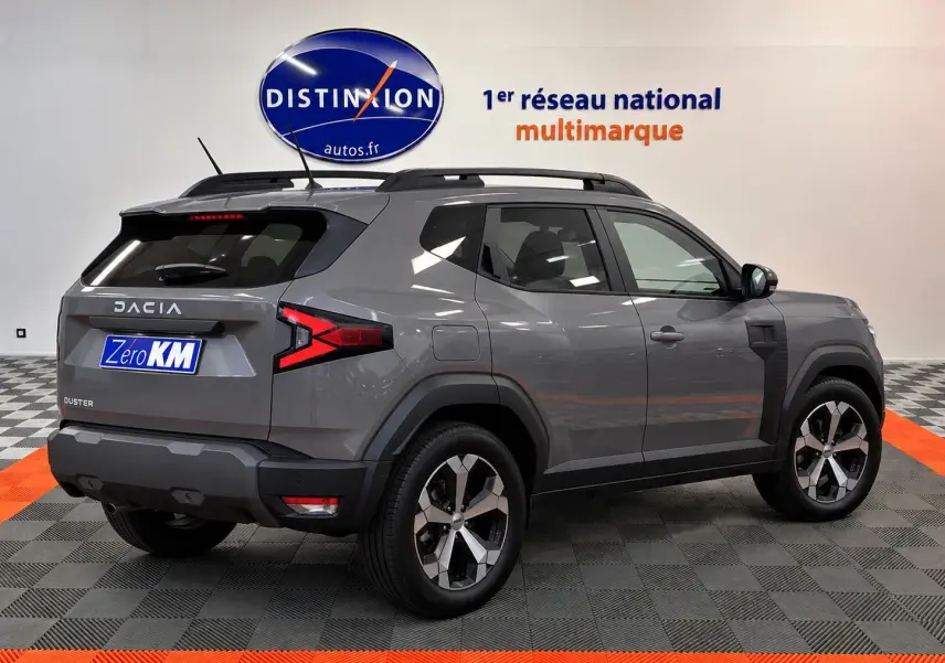 Vue 3/4 arrière droite du Dacia Duster gris schiste 2026 avec jantes alliage et barres de toit noires.
