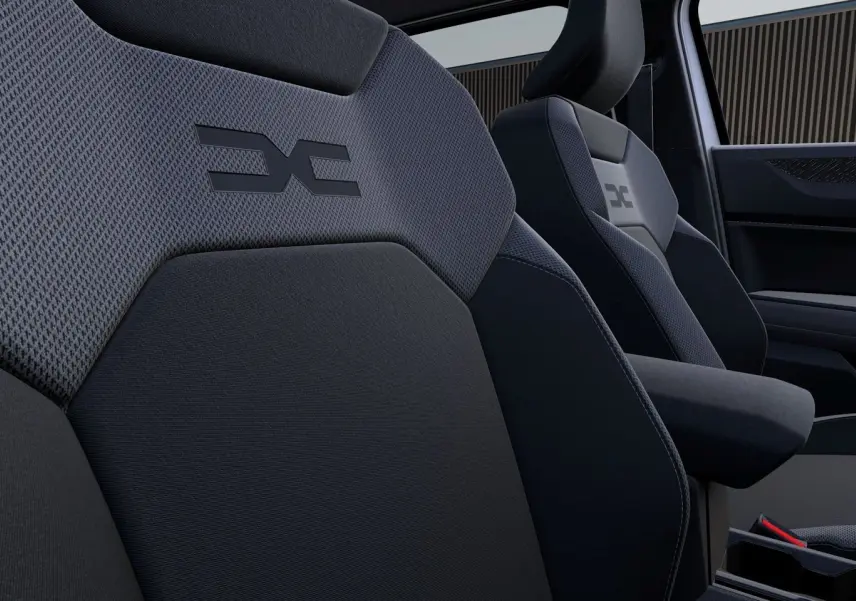 Gros plan sur les sièges avant gris foncé du Dacia Duster 2026 avec logo distinctif brodé sur les appuie-têtes.