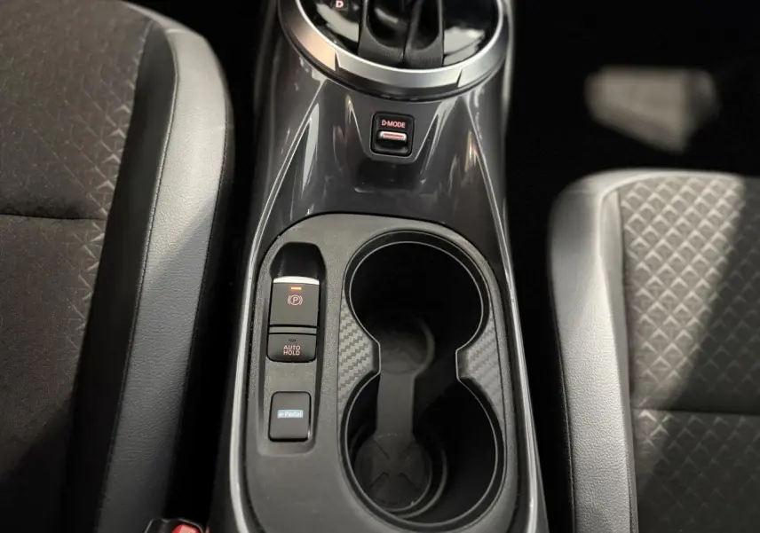 Gros plan sur la console centrale noire du Nissan Juke Hybrid 2024 avec porte-gobelets et commandes e-Pedal et frein électrique.