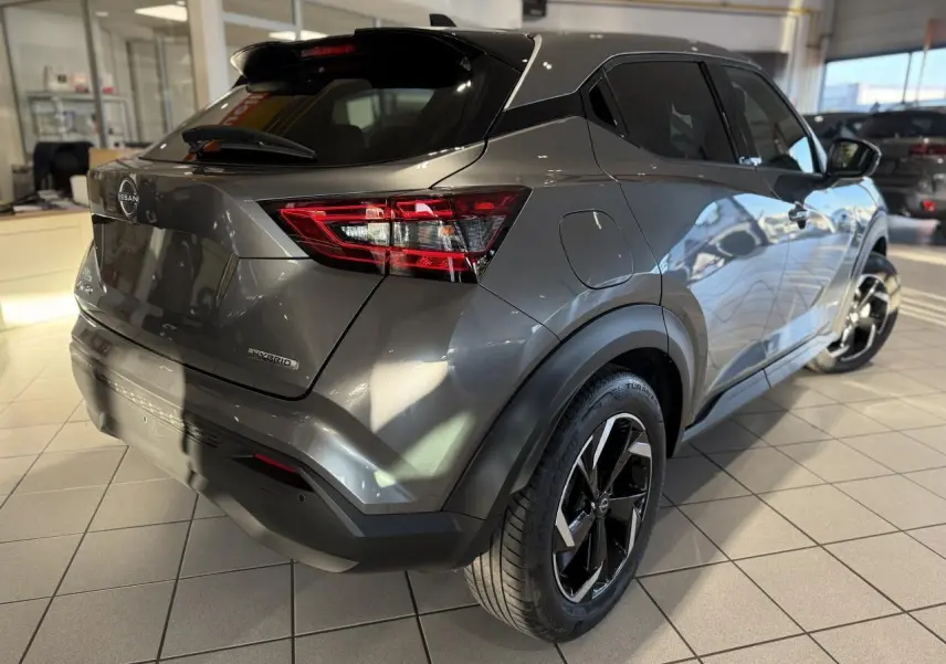 Vue 3/4 arrière droit du Nissan Juke Hybrid gris métallisé avec jantes alliage noires en showroom.