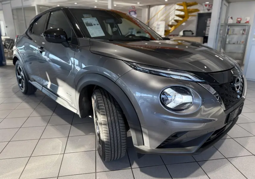 Nissan Juke Hybrid gris métallisé en 3/4 avant droit, avec phares LED et calandre noire en showroom.