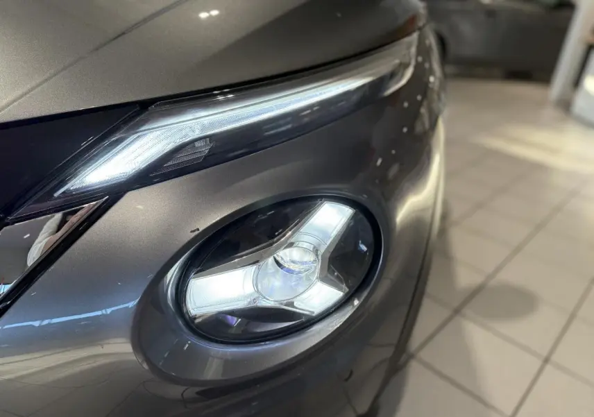 Gros plan sur le phare avant droit allumé du Nissan Juke Hybrid gris métallisé, mettant en valeur son design LED distinctif.