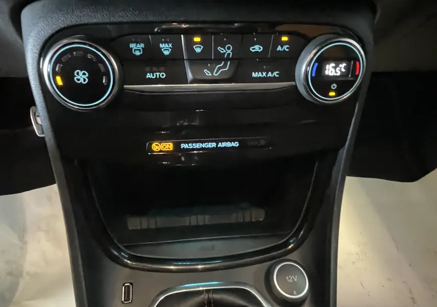 Vue rapprochée de la console centrale du Ford Puma gris, montrant les commandes de climatisation et l'indicateur d'airbag passager.