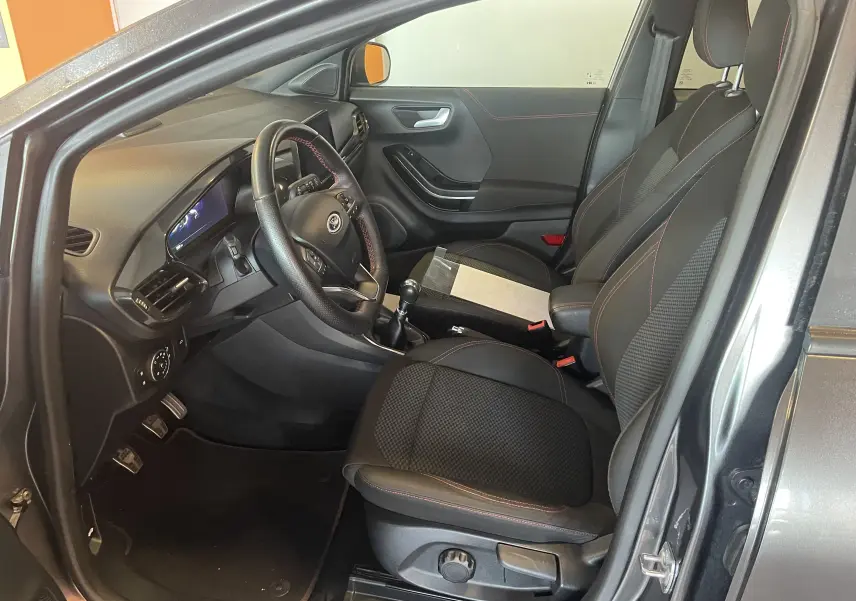 Intérieur avant droit du Ford Puma gris 2020, sièges noirs avec surpiqûres rouges et volant multifonction en cuir.