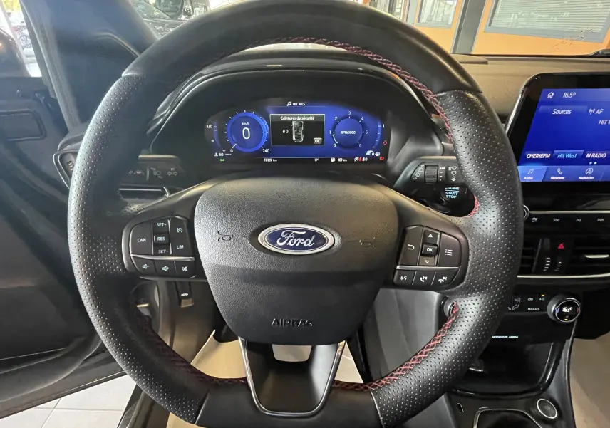 Vue centrée sur le volant noir avec surpiqûres rouges du Ford Puma 2020, tableau de bord numérique et écran tactile visible.