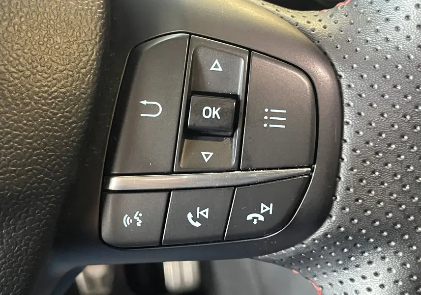 Gros plan sur les commandes multifonctions noires du volant perforé avec surpiqûres rouges du Ford Puma gris 2020.