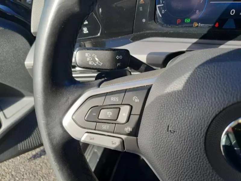 Gros plan sur le volant cuir noir de la Volkswagen Golf 1.5 eTSI, avec commandes multifonctions côté gauche et tableau de bord numérique.