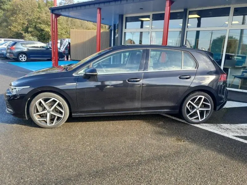 Profil côté gauche d'une Volkswagen Golf noire nacrée 2021 avec jantes alu 18 pouces au stationnement extérieur.