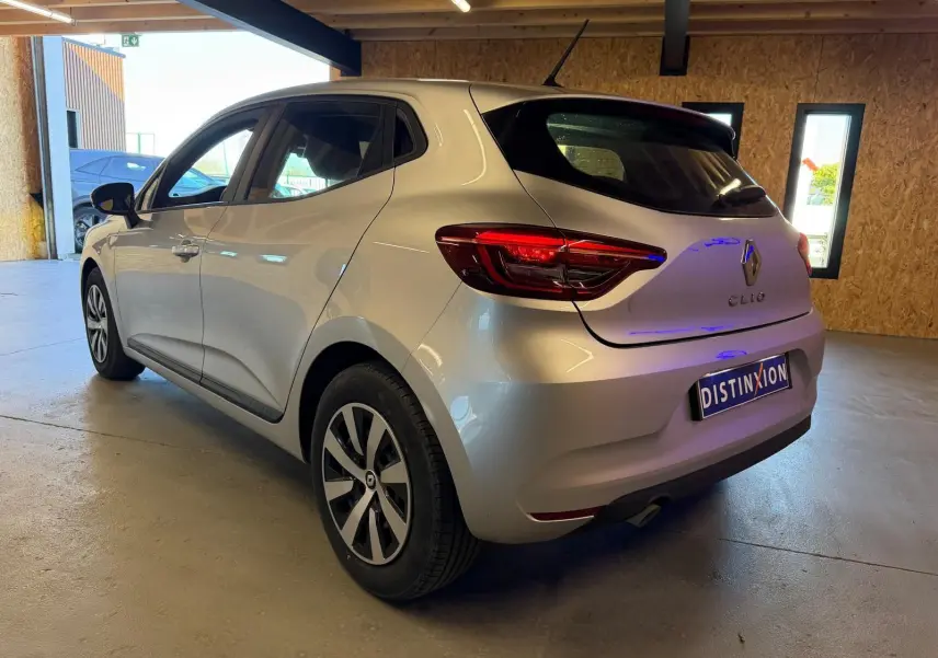 Vue 3/4 arrière droite d'une Renault Clio gris platine 2023 avec feux arrière LED et becquet dans un garage.