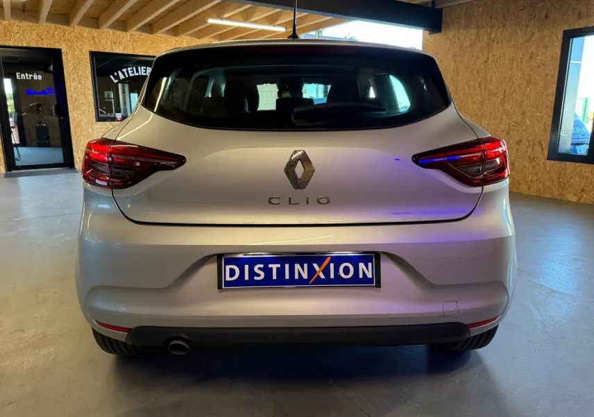Vue arrière d'une Renault Clio gris platine 2023 avec feux arrière LED et becquet, en intérieur showroom.