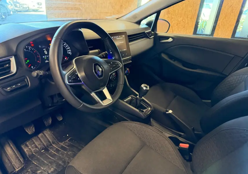 Vue intérieure côté conducteur de la Renault Clio gris platine 2023, volant multifonction et écran tactile central visible.