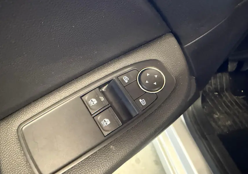 Gros plan sur les commandes de vitres électriques et rétroviseurs côté conducteur d’une Renault Clio gris platine.