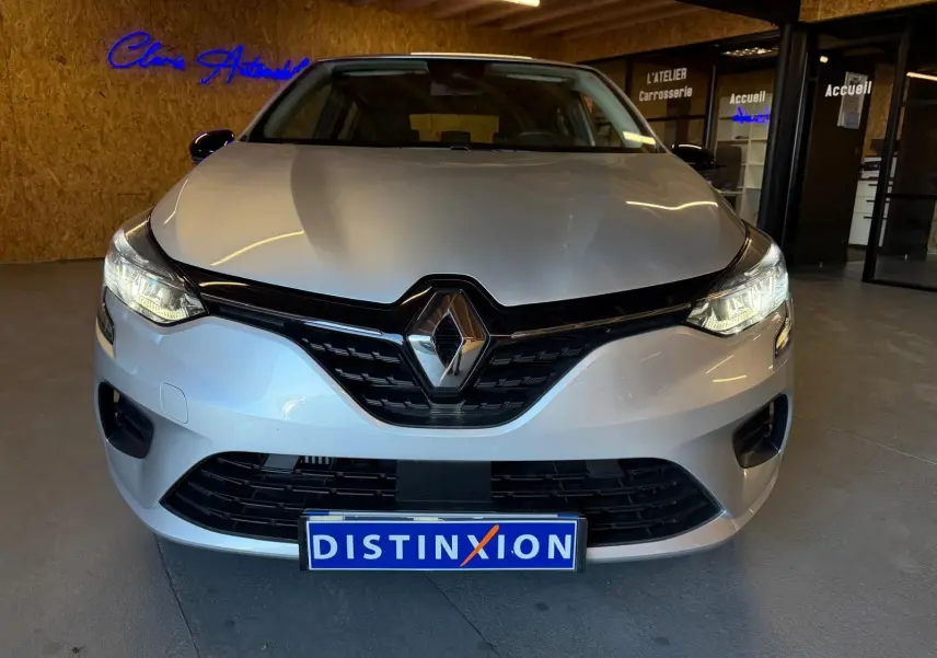 Vue avant d'une Renault Clio 1.0 TCE 90 Équilibre gris platine avec phares allumés en intérieur showroom.