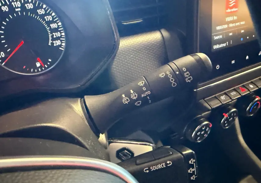 Détail intérieur du tableau de bord côté gauche de la Renault Clio gris platine 2023, avec commandes essuie-glaces et écran tactile.